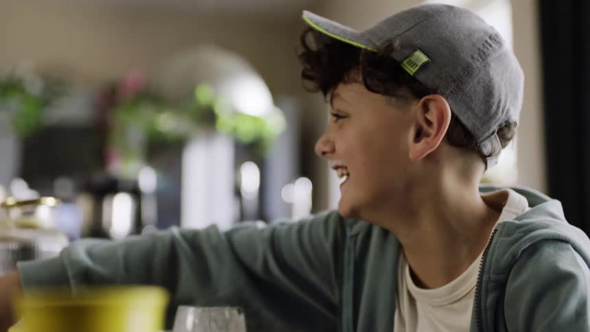 Two young teenagers laugh and play at a cluttered kitchen table filled with food