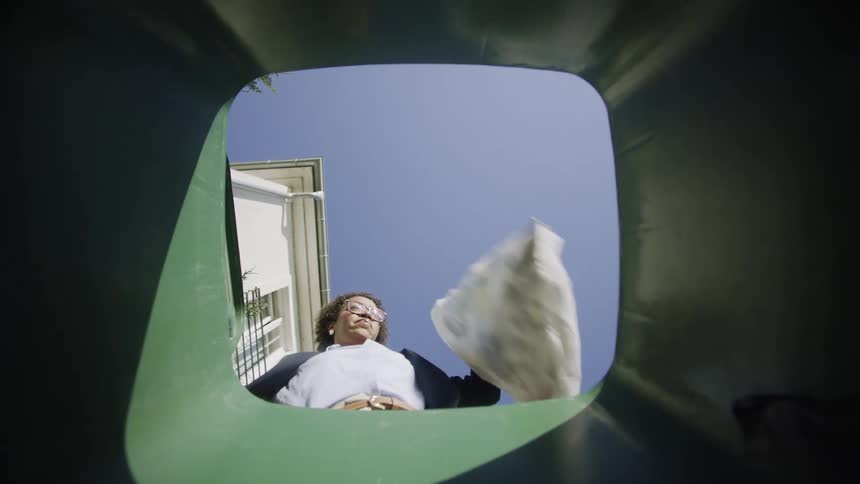 Woman drops trash into a bin seen from the inside looking up