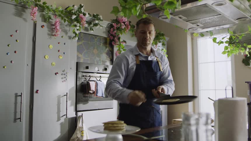 A man flips pancakes on a pan over the stove