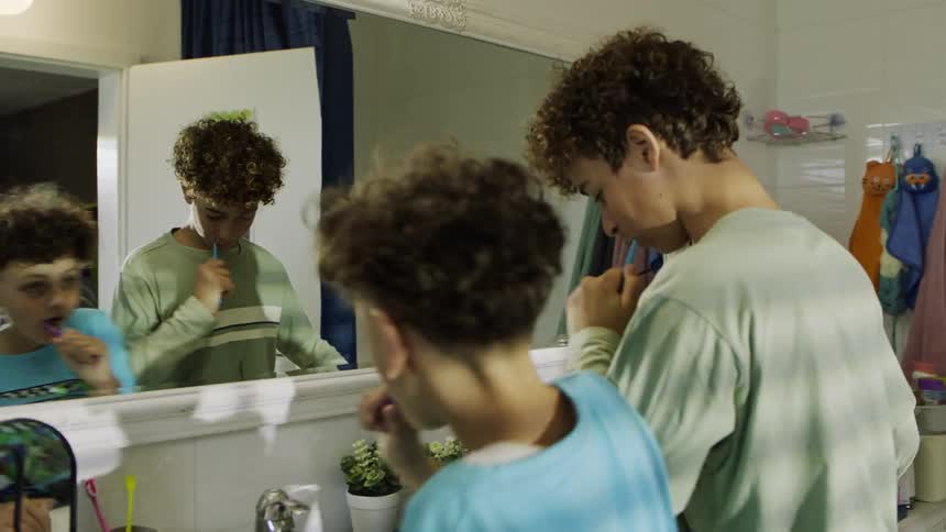 Two brothers playfully brush their teeth together in a bathroom as one teases the other
