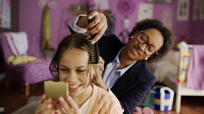 A girl looks in a mirror as her mother brushes her hair