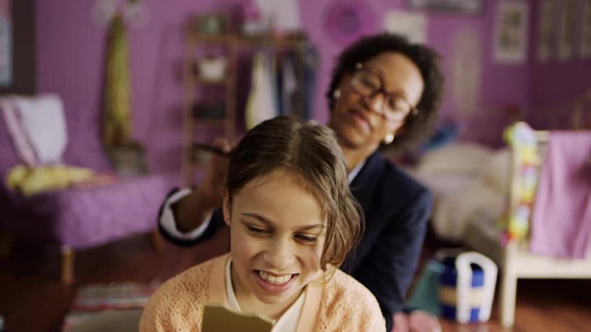 A little girl is happy while her mother is fixing her hair using a comb