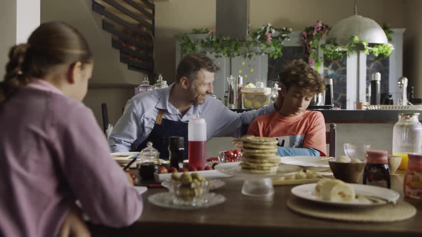 Father serves pancakes then joins his family for breakfast