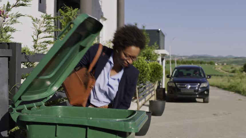 Woman taking out trash bags to trash can outside front porch then walking to her car