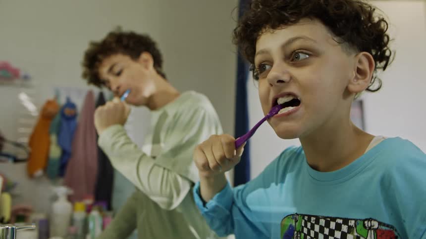 Two boys brush their teeth together at the bathroom sink