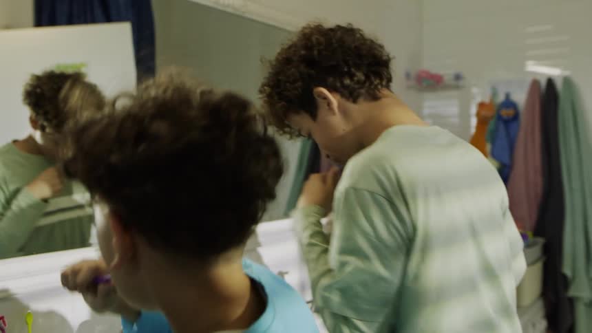 Two kids brush their teeth and play while facing a mirror in the bathroom