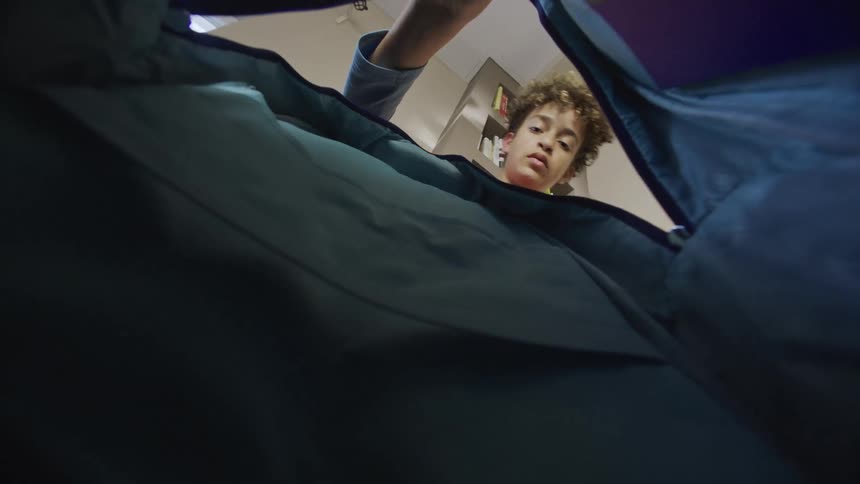 Boy packs his backpack in his bedroom with a serious expression on his face