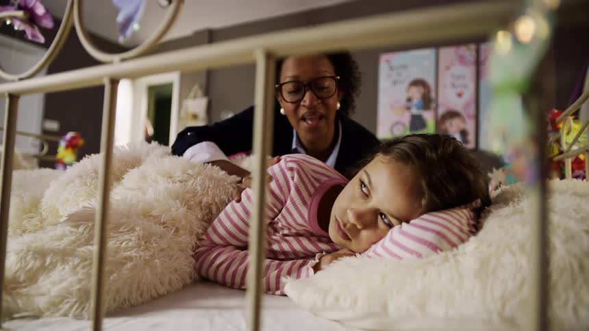 Mother gently wakes up her daughter with a smile in a cozy bedroom