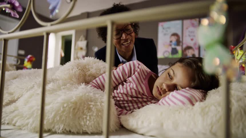 A mother walks into a bedroom where her child is sleeping and wakes her up sparking excitement as the mother kisses her