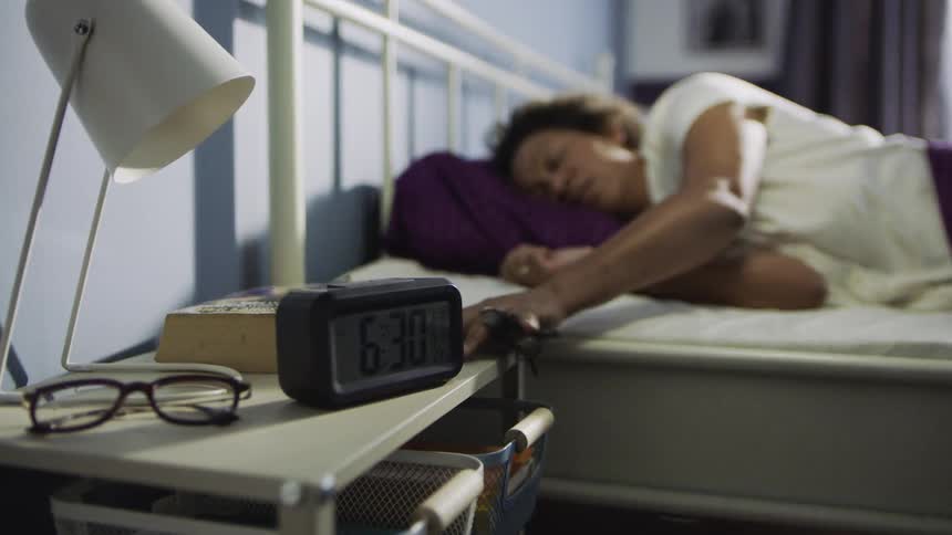Woman reaches to turn off alarm clock while waking up in bed