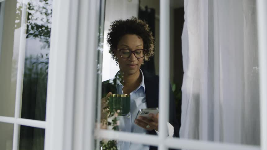The woman checks her phone and drinks coffee inside