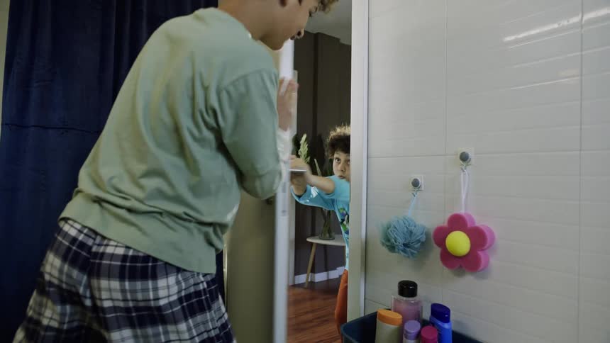 A boy tries to prevent his brother from entering into the bathroom