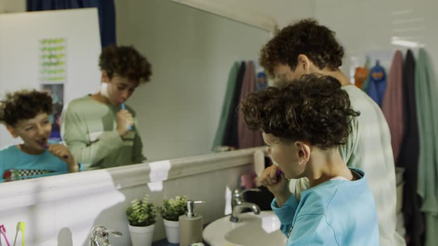 Two teenage brothers play while brushing their teeth at the sink in the bathroom