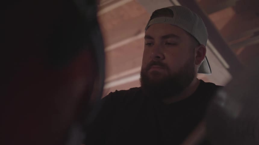 A closeup of a bearded man in a cap playing drums inside a dimly lit garage