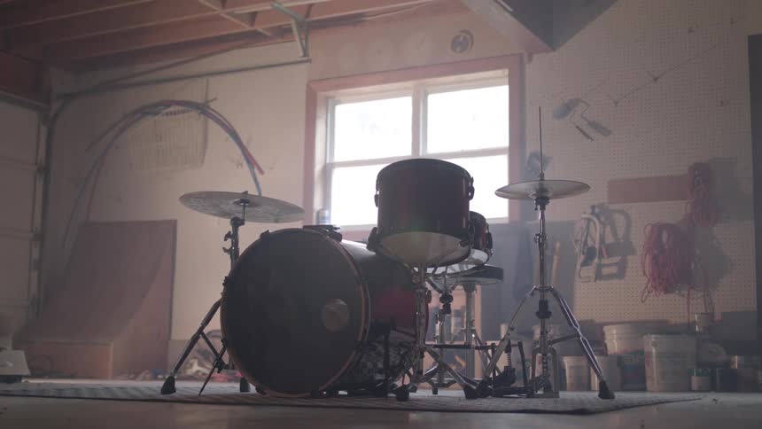A drum kit sits in a cluttered garage workshop surrounded by tools cords and shelves of hardware