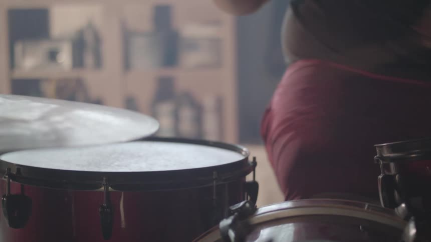 A closeup shot of a person playing a drum with visible movement of the drumstick