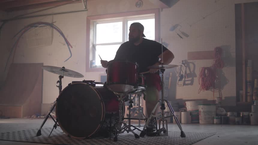 A man plays a drum set alone in a dimly lit garage