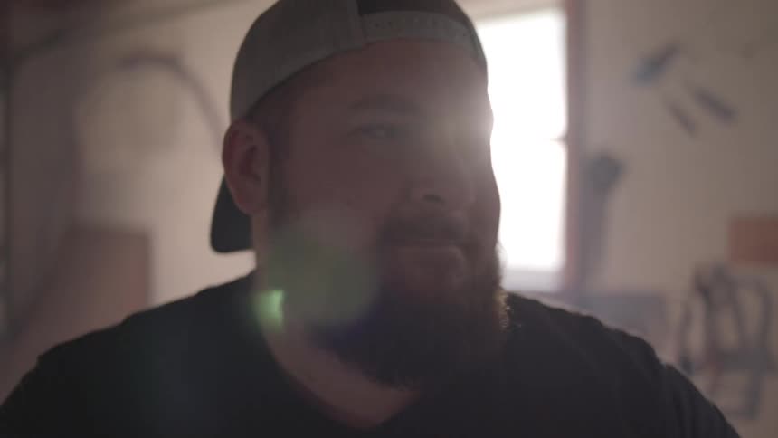 A closeup of a man in a cap playing drums with drumsticks inside a garage