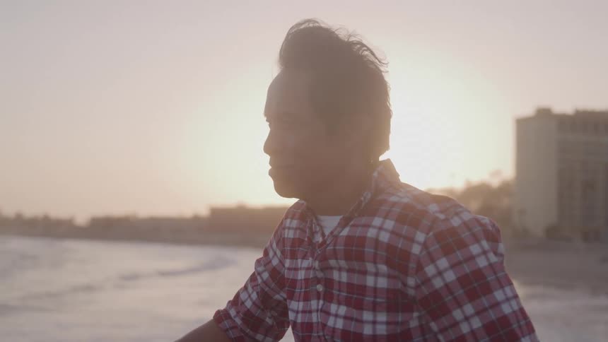 Man gazes thoughtfully at the ocean during sunset from a seaside location