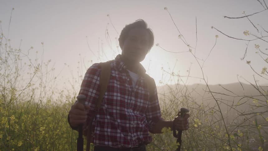 Man hiking through tall wildflowers at sunset