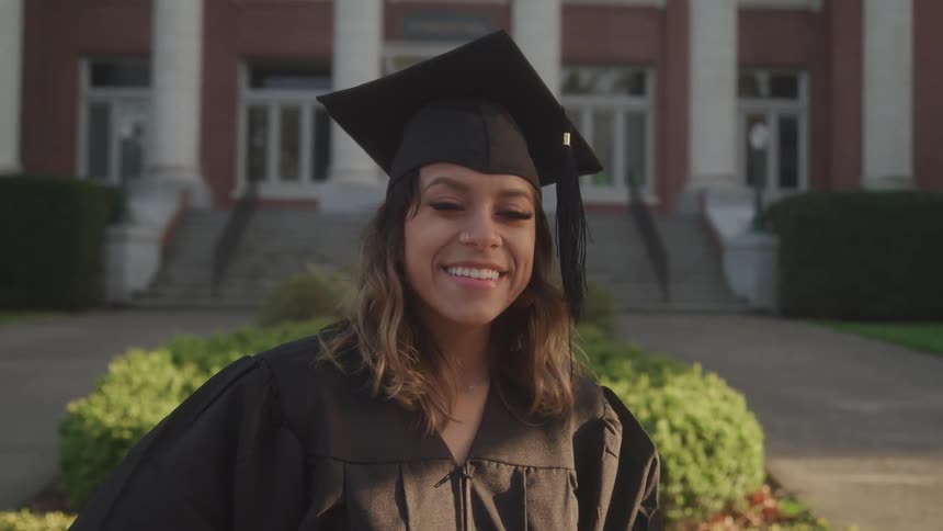 The graduate is standing outside the school smiling