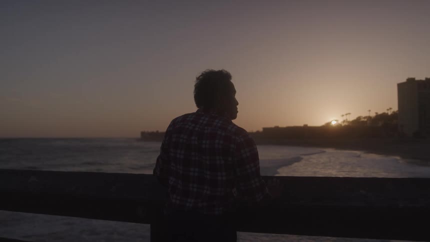 Back of a man standing on the pier looking at the ocean at sunset