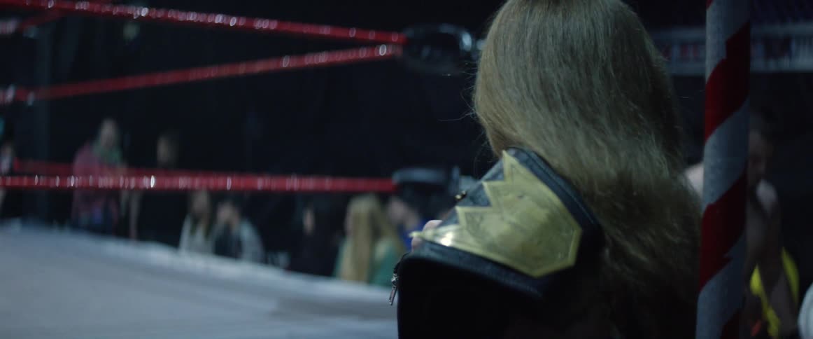 A woman looks in from outside a ring holding a championship belt