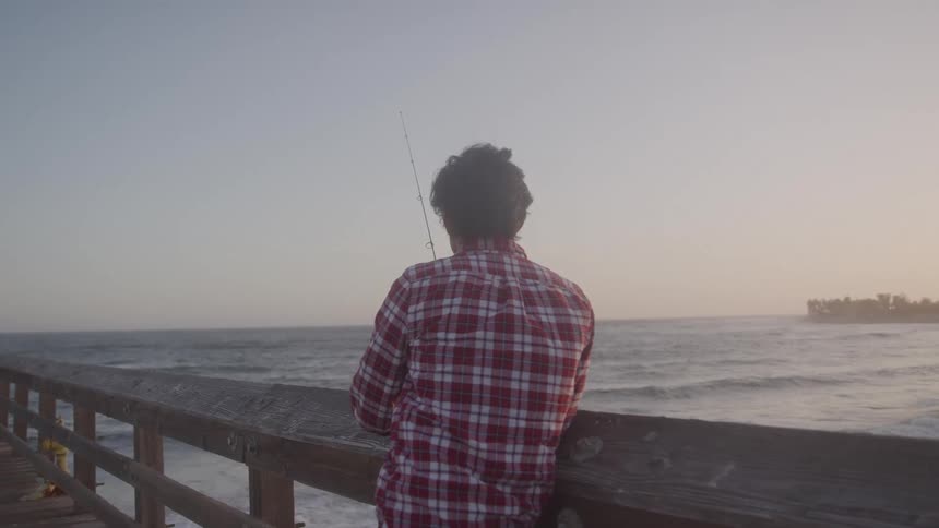 Man fishes alone on a pier at sunset