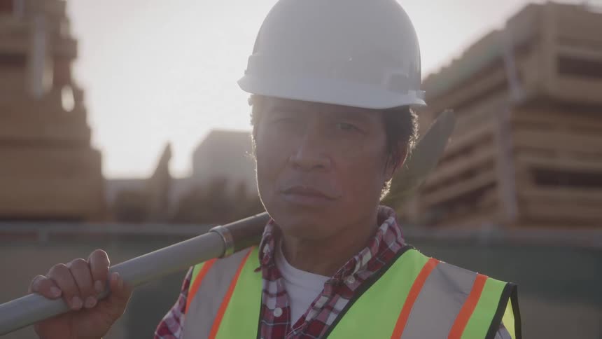 Construction worker holds pole on shoulder at worksite