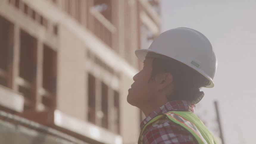 A construction worker in a hard hat looks up at a building under construction