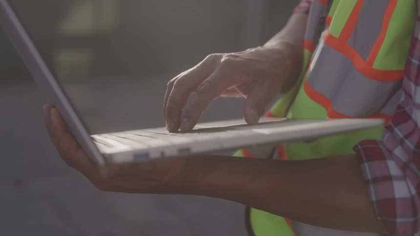 A construction worker uses a laptop while wearing a safety vest