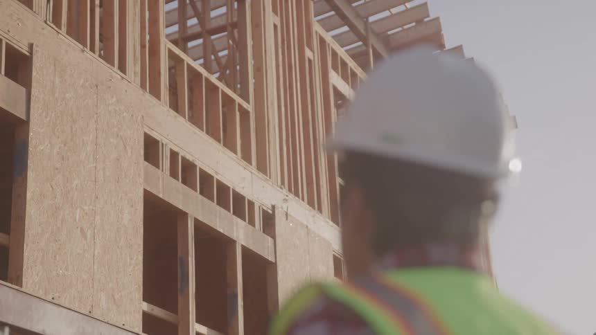 Man wearing a helmet and protective gear observing the outside of a building under construction