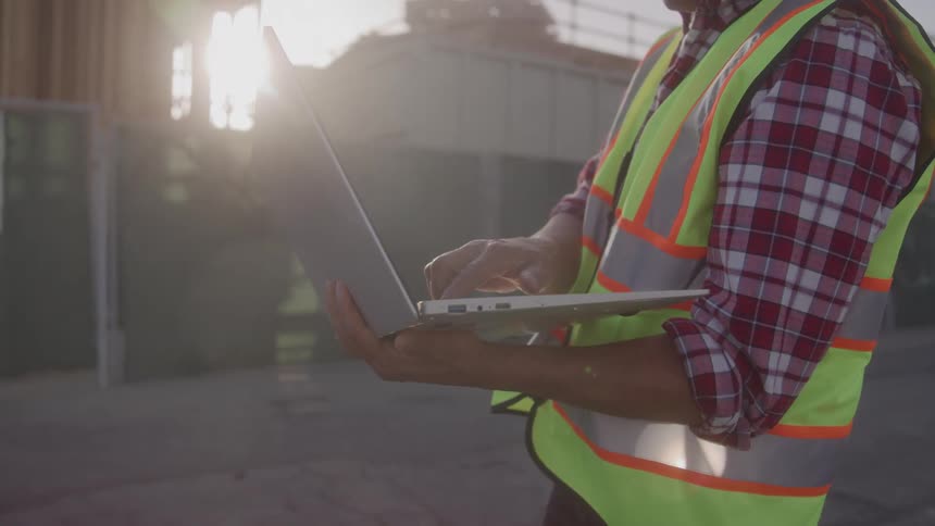 The worker is holding a laptop near the work site
