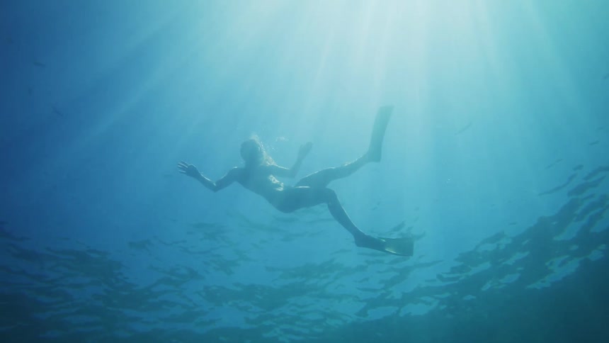A person wearing duck feet is diving underwater near the surface where a ray of sunlight is coming from