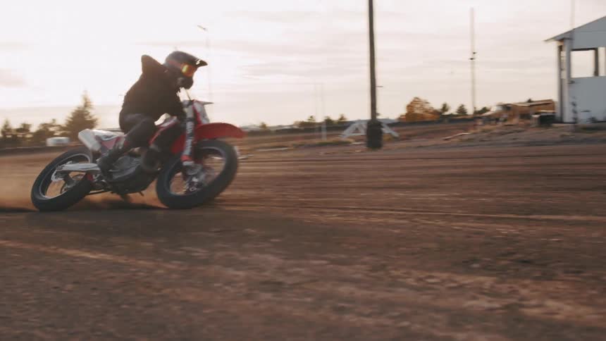 A person drifts a motorcycle on a dirt track kicking up dust
