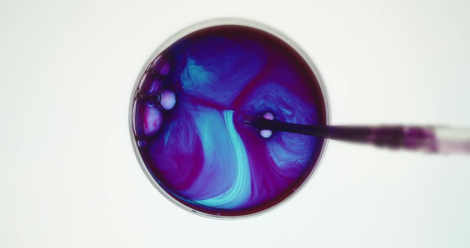 A pipette stirs a blue liquid turning it purple