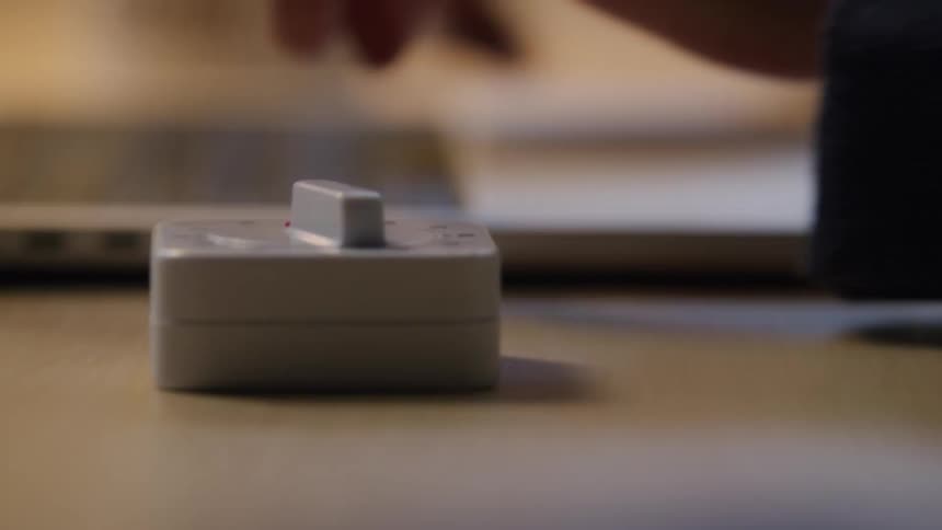A person sets a timer on the desk beside them before starting to type on a laptop