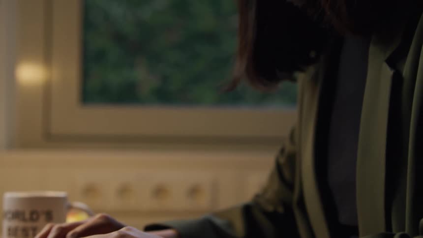 A woman is typing on a laptop at a desk with a coffee mug nearby