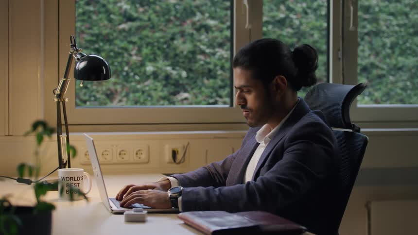 Tired man in business attire claps his face and stretches at desk to stay awake
