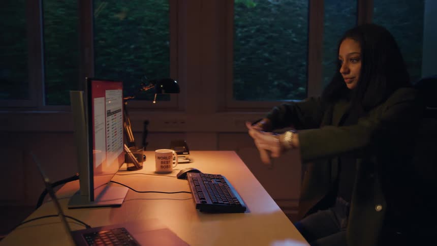 Woman sitting at an office desk at night and typing on a computer keyboard