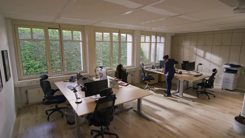 A man and a woman dressed in formal wear are in a large office with tables and computers