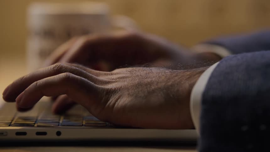 Hands type on a laptop keyboard beside a coffee mug on desk
