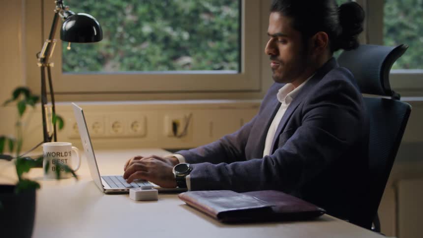 A man sits in an office typing and slapping his face to stay awake