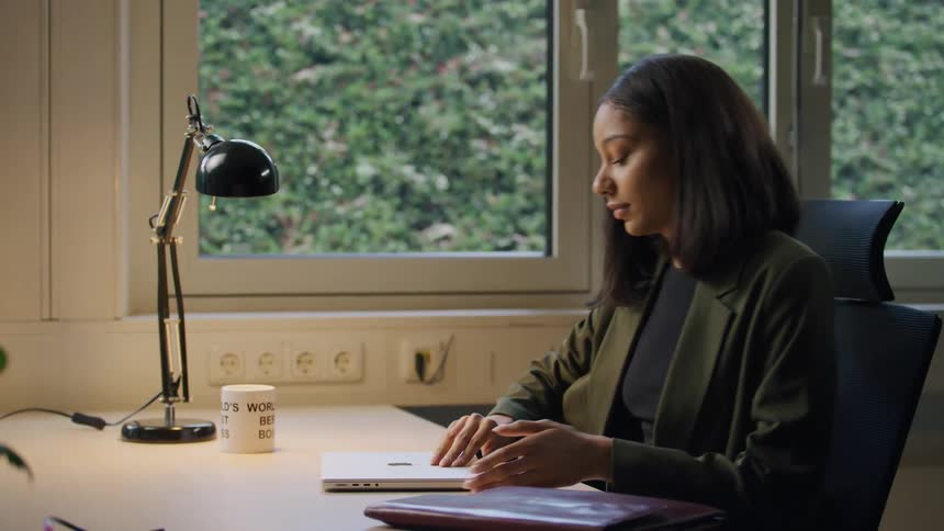 Lady sits on a office chair switched on the lamp opened the laptop and started typing