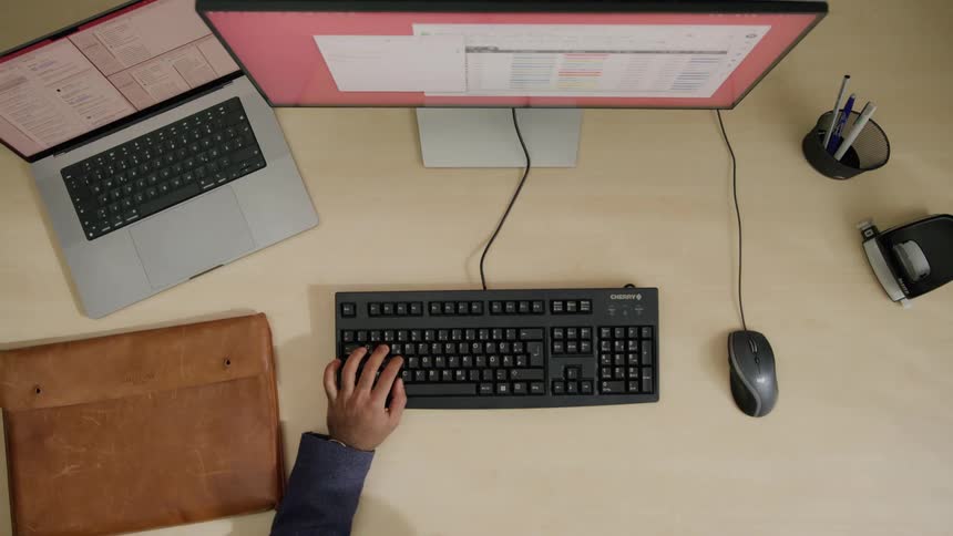 Man drinks beverage from a cup while working with a computer on an office table