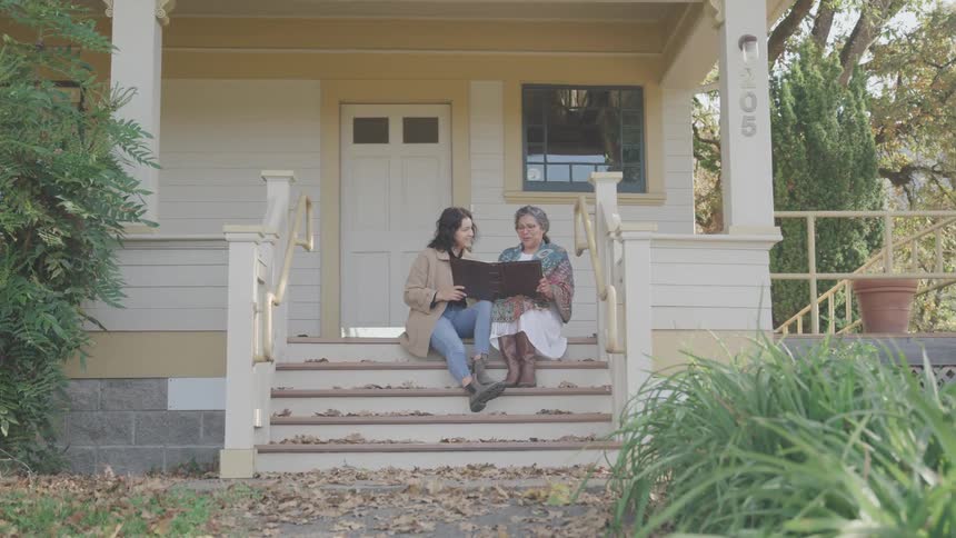 Elderly woman and woman sitting outside a house on the steps reading a book