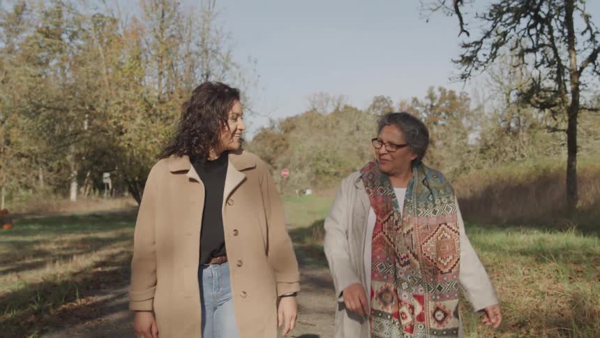 A younger woman and an older woman walk and talk together on a country path on a sunny autumn day
