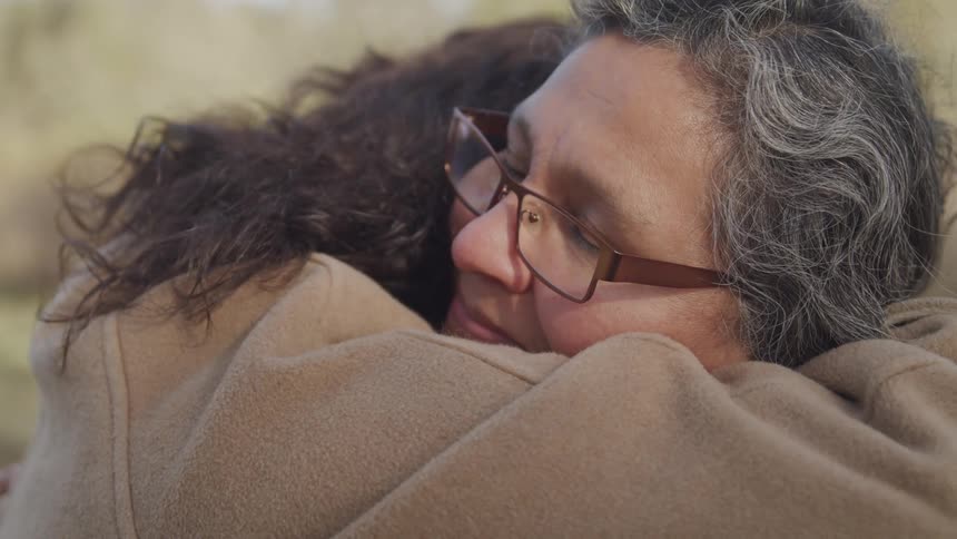 Older woman smiles while being hugged by a younger woman