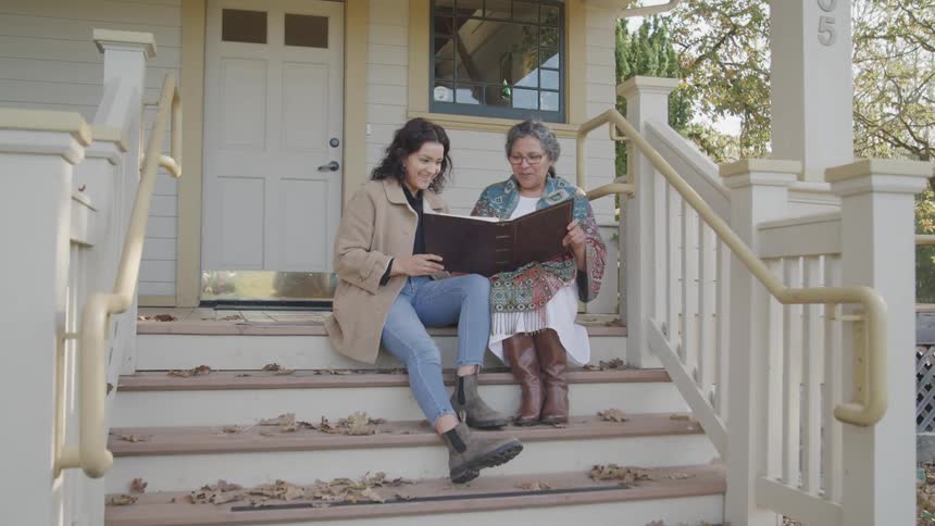Two women are looking at a photo album on the steps