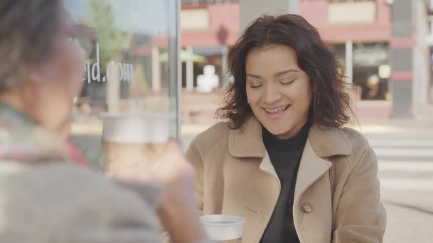 A mother and daughter share a warm conversation over coffee at an outdoor caf